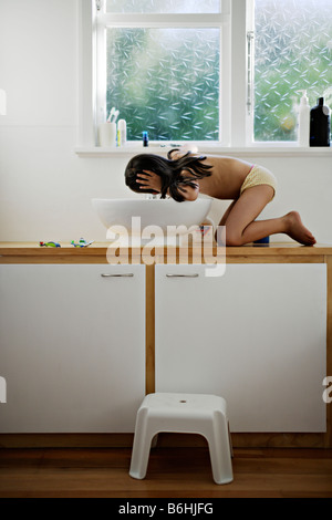 Petite fille de cinq ans monte jusqu'à la salle de bains lavabo pour boire l'eau du robinet Banque D'Images