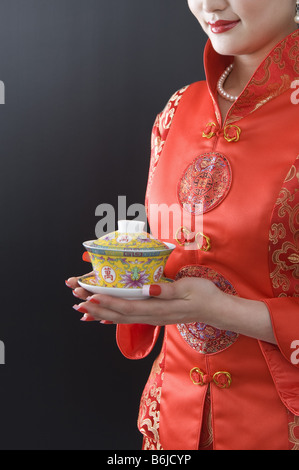 Jeune femme portant un qipao traditionnelle chinoise tenant une tasse de thé traditionnelles avec les deux mains Banque D'Images