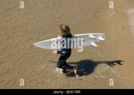 Les jeunes adolescents de sexe masculin de l'eau transportant de surf surfeur entrant Banque D'Images