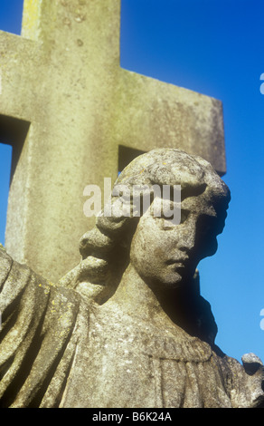 Détail de la pierre calcaire pierre tombale angel de la tête et des épaules en lumière chaude avec grande pierre crucifix derrière Banque D'Images