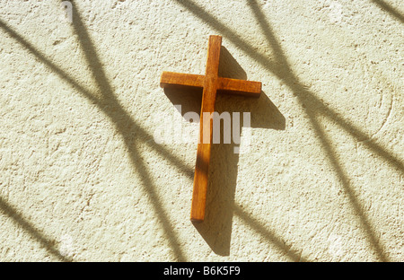 Petit crucifix en bois couché dans la lumière du soleil sur le rebord de pierre brute peint en crème avec des ombres de diamant clair Verre au plomb Banque D'Images