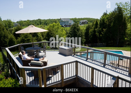 Dame de détente sur une terrasse en bois moderne avec parapluie bleu surplombant une piscine dans la cour arrière d'une banlieue moderne accueil Banque D'Images