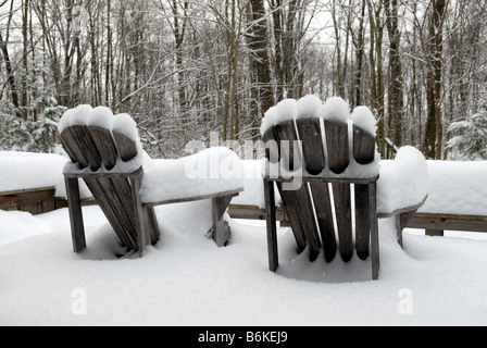 Scène d'hiver, montrant Muskoka/chaises Adirondack laissés sur le pont couvert de chalets d'été avec de la neige profonde, à la recherche sur la forêt. Banque D'Images