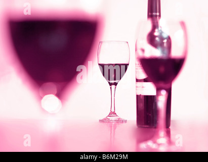 Un verre de vin rouge sur un tableau encadré par d'autres problèmes de mise au point des verres et une bouteille Banque D'Images