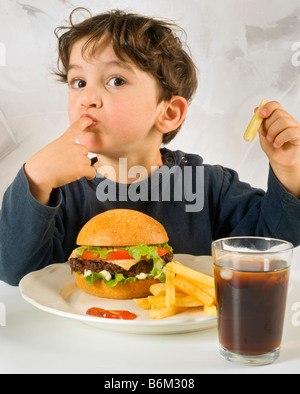 Jeune garçon mangeant chessburger avec frites et Coca Banque D'Images