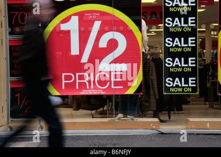 Homme marchant passé moitié prix vente signes de réduction dans une vitrine sur un uk high street à Belfast en Irlande du Nord Banque D'Images