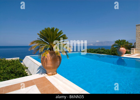 Piscine à débordement privée exclusive de luxe invitant un plongeon, donnant sur la mer Egée avec palmiers et urnes grecques typiques Banque D'Images