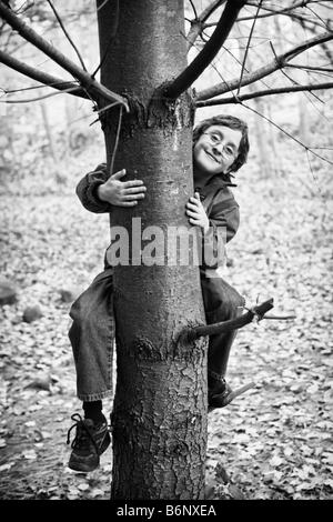 Image en noir et blanc du jeune garçon escalade un arbre, souriant à la caméra dans l'auto-suffisance satisfction Banque D'Images