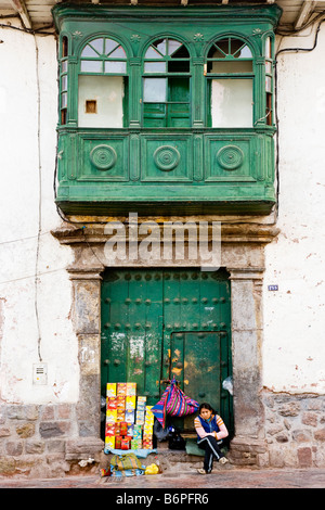 Jeune femme péruvienne qui vendent des marchandises en porte de maison coloniale espagnole dans une rue latérale à Cusco, Pérou, Amérique du Sud Banque D'Images