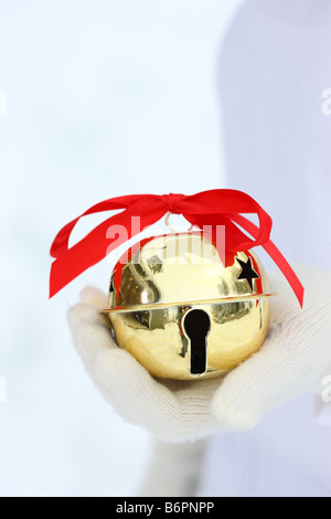 Les mains avec des gants hiver holding Christmas Jingle Bell avec red bow Banque D'Images