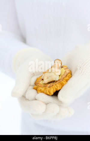 Les mains avec des gants hiver holding Baby Jesus nativité figure Banque D'Images