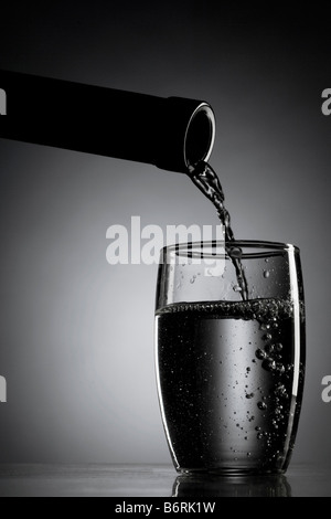 On verse de l'eau de la bouteille au verre éclairé par LED Banque D'Images