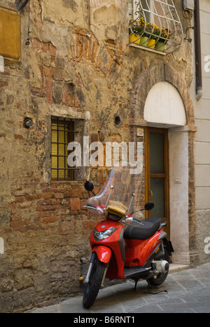 Scooter rouge garée à l'extérieur une maison typique à Sienne, Toscane, Italie. Au-dessus est un balcon avec des plantes en pot peu colorées alignées Banque D'Images