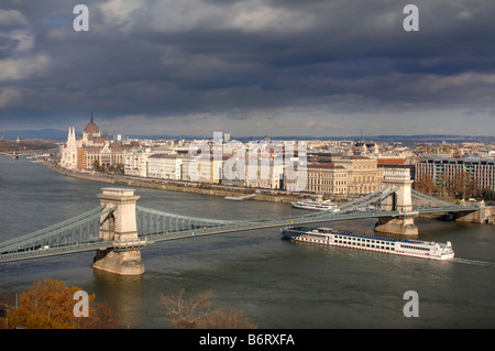 Une BARGE TOURISTIQUE PASSE SOUS LE PONT DES CHAÎNES AVEC LE PARLEMENT DE LA DISTANCE SUR LA RIVE DU DANUBE DANS Banque D'Images