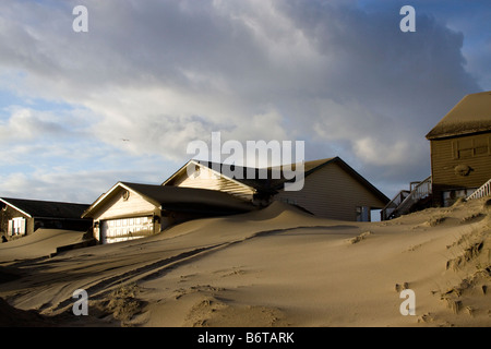 Dunes de sable hautes de pieux contre residences après une tempête hivernale sur la côte de l'Oregon. Banque D'Images