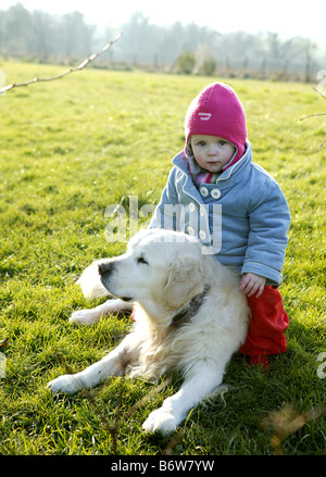 Petit enfant espiègle se trouve au sommet d'un golden retriever dog dans le jardin pendant la saison d'hiver Banque D'Images