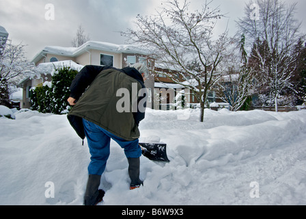 Homme creuser la neige de bord de route défoncée de glace en face de la maison après le big tempête Banque D'Images