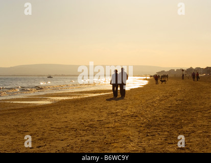 Un couple en train de marcher sur la plage de Bournemouth au coucher du soleil. Le Dorset. UK. Banque D'Images