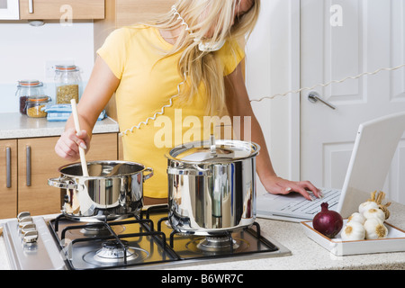 La cuisine femme tandis que le téléphone portable et l'utilisation Banque D'Images