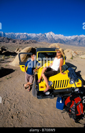 L'homme et la femme traînant sur le capot d'une jeep dans le désert, à côté de la montagne. Banque D'Images