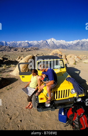 L'homme et la femme traînant sur le capot d'une jeep dans le désert, à côté de la montagne. Banque D'Images