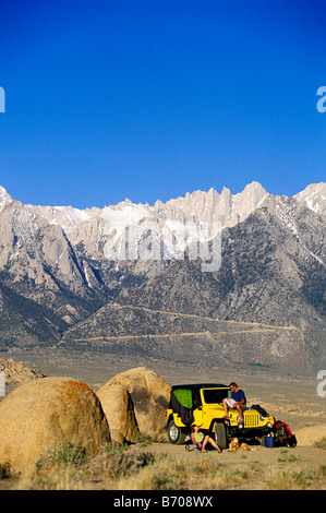 L'homme et la femme traînant à côté d'une jeep dans le désert avec des montagnes en arrière-plan. Banque D'Images