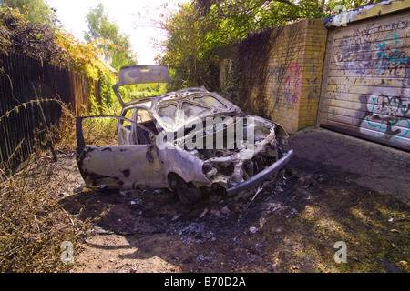 Voiture brûlée et graffiti sur porte de garage à alley près de maisons résidentielles Banque D'Images