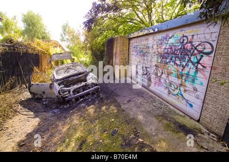 Voiture brûlée et graffiti sur porte de garage à alley près de maisons résidentielles Banque D'Images