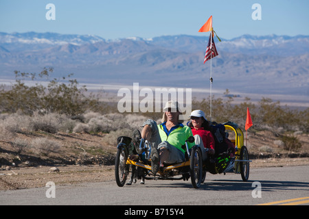 Un homme et une femme leur pédale vélo tandem avec leur chien le long de côte sur une route du désert de Mojave en dehors de Randsburg CA Banque D'Images