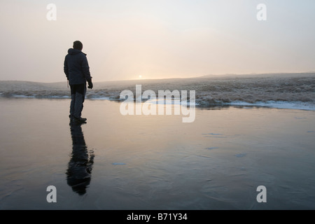 Un marcheur sur un tarn gelé près du sommet d'Caudale Moor dans le Lake District UK Banque D'Images