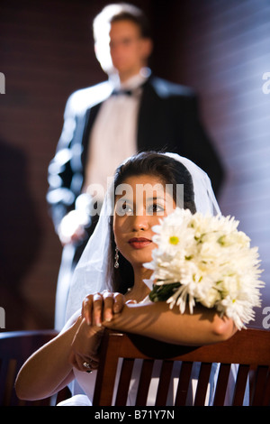 Young Asian bride posing with bouquet, marié à l'arrière-plan Banque D'Images