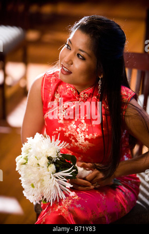 Young Asian Woman in traditional dress sitting in chair et holding bouquet floral Banque D'Images