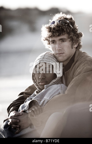 Image en noir et blanc de jeunes l'interracial couple sitting on beach avec bras autour de Banque D'Images