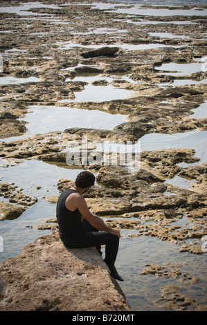 Homme seul assis sur la roche par la mer Banque D'Images