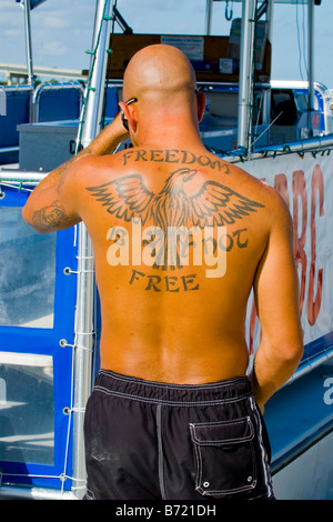 Marina de voilier sun chauve jeune homme bronzé en maillot de bain avec le tatouage en disant la liberté n'est pas un aigle ronde libre Banque D'Images