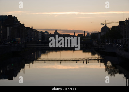 Coucher de soleil sur la Liffey à Dublin, Irlande.Horizon montre aux gens de traverser un pont et leur reflet dans l'eau. Banque D'Images