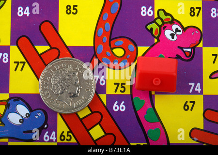 Pièce d'une livre et toy red house sur une carte de serpents et échelles avec des livres sur l'échelle et de la chambre sur le serpent Banque D'Images