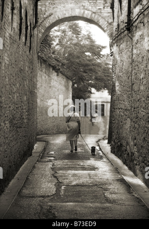 Une femme promener son chien sur une route en pierre par un ancien porche à Pérouse, Italie Banque D'Images
