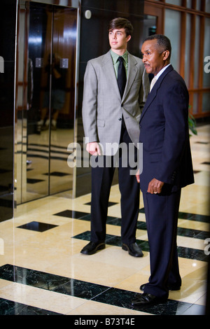 Homme d'origine afro-américaine avec jeune collègue en attente d'ascenseur Banque D'Images