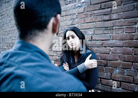 Young Hispanic couple parle en dehors appuyé contre un mur de briques Banque D'Images