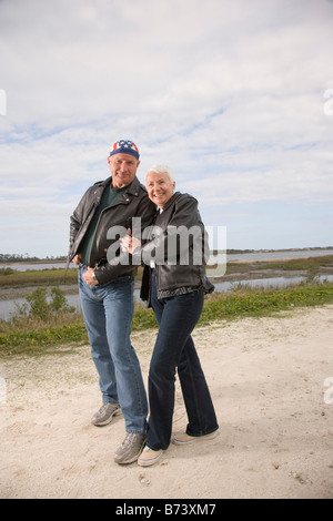 Portrait of happy senior couple in biker jackets standing on dirt road Banque D'Images