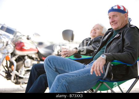 Happy senior couple motard assis sur des chaises à côté de motorcycle Banque D'Images
