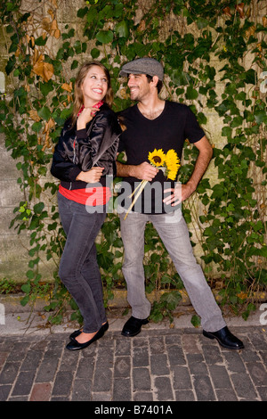 Jeune couple posant devant un mur couvert de lierre, holding tournesols jaunes Banque D'Images