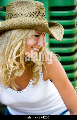 Portrait of young girl in cowboy hat assis sur le tracteur à l'extérieur Banque D'Images