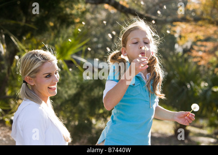 Mère et fille en parc, daughter blowing dandelion seeds Banque D'Images