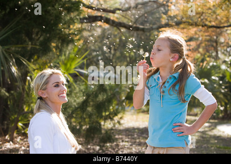 Mère et fille en parc, daughter blowing dandelion seeds Banque D'Images