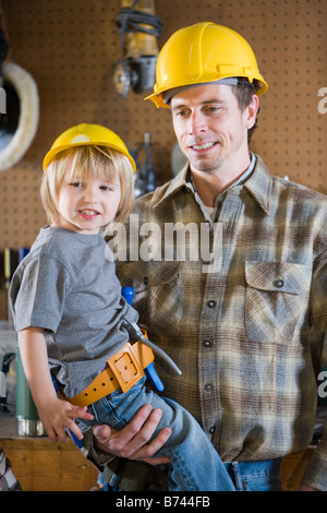 Portrait de père et fils en garage wearing hard hats Banque D'Images