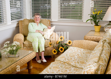 Portrait d'une femme âgée assise sur chaise en osier dans la salle de séjour Banque D'Images