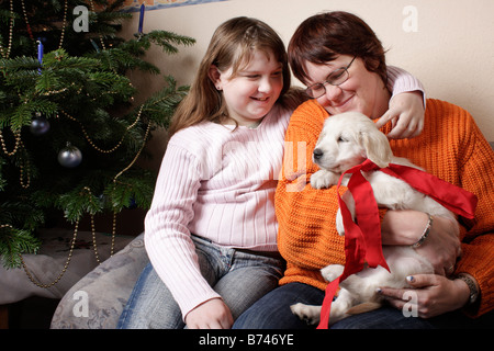 Mère et fille de câliner nouveau pup heureusement en face de leur arbre de Noël Banque D'Images