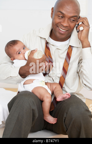 Père de l'Afrique de nourrir bébé fille et talking on cell phone Banque D'Images